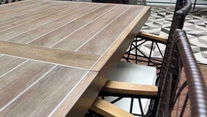 Een terras met een houten tafel, stoelen, een barbecue en een bakstenen muur.