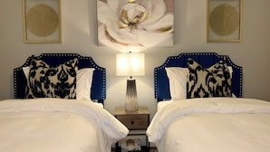 Een hotelkamer met twee bedden, een nachtkastje, een lamp en twee kunstwerken in een lijst aan de muur.