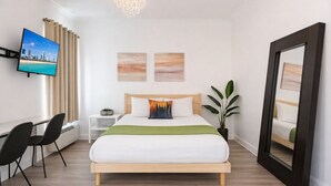 Et moderne hotelværelse med seng, skrivebord, stol, fjernsyn og kunst på væggene.