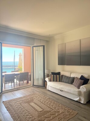 A living room with a white sofa, a patterned rug, and a view of the sea through a sliding glass door. - Sea view one bedroom apartment in Lustica Marina (Radovići)