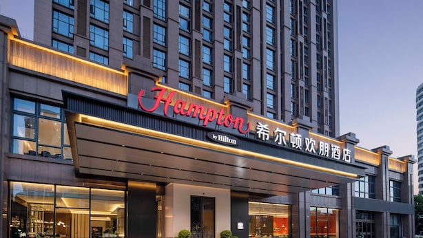 Een modern hotel met een opvallend 'Hampton by Hilton' bord, grote ramen en een goed verlichte ingang.