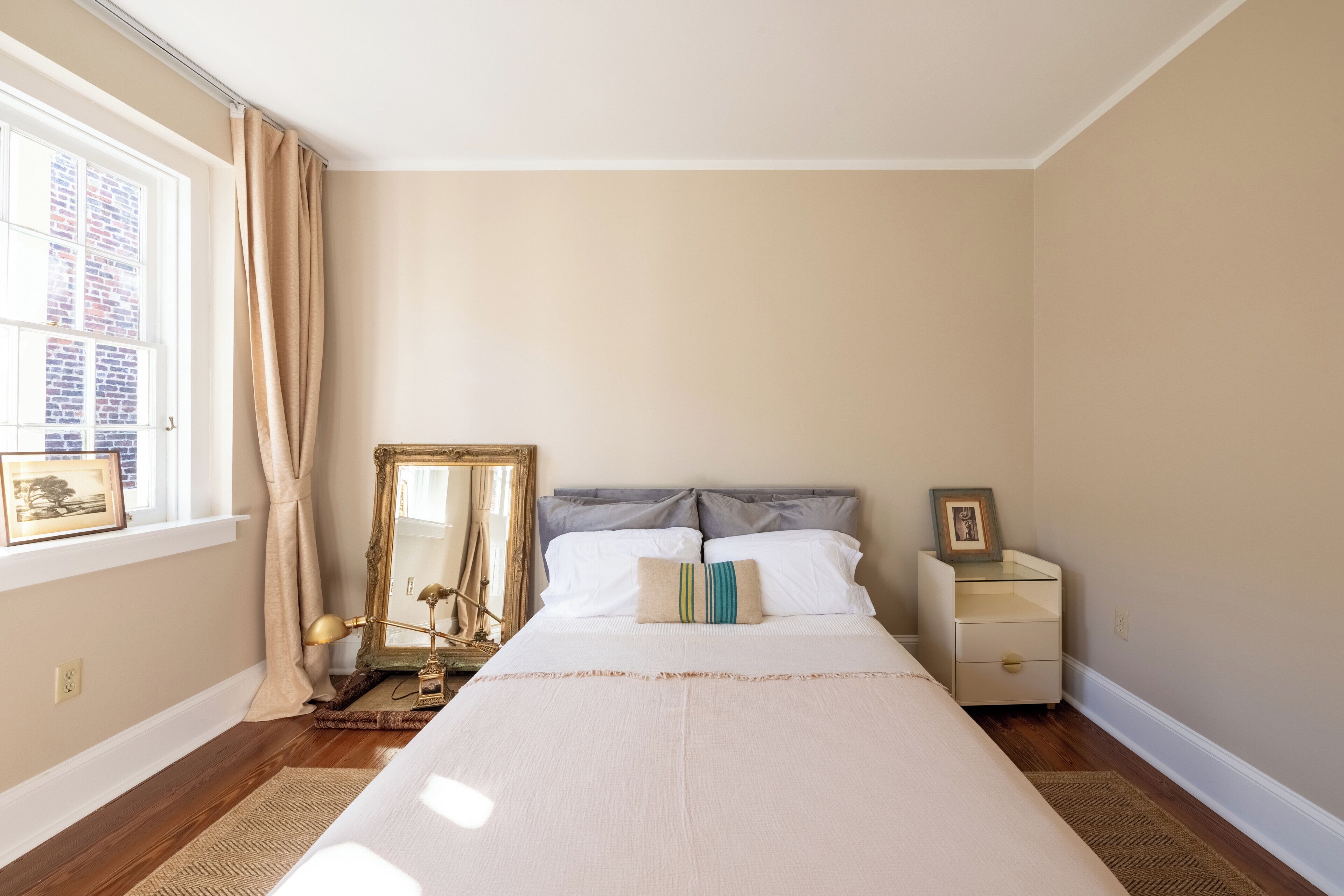 A bedroom with a large bed, a nightstand, a mirror, and a window with curtains.
