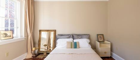 A bedroom with a large bed, a nightstand, a mirror, and a window with curtains.