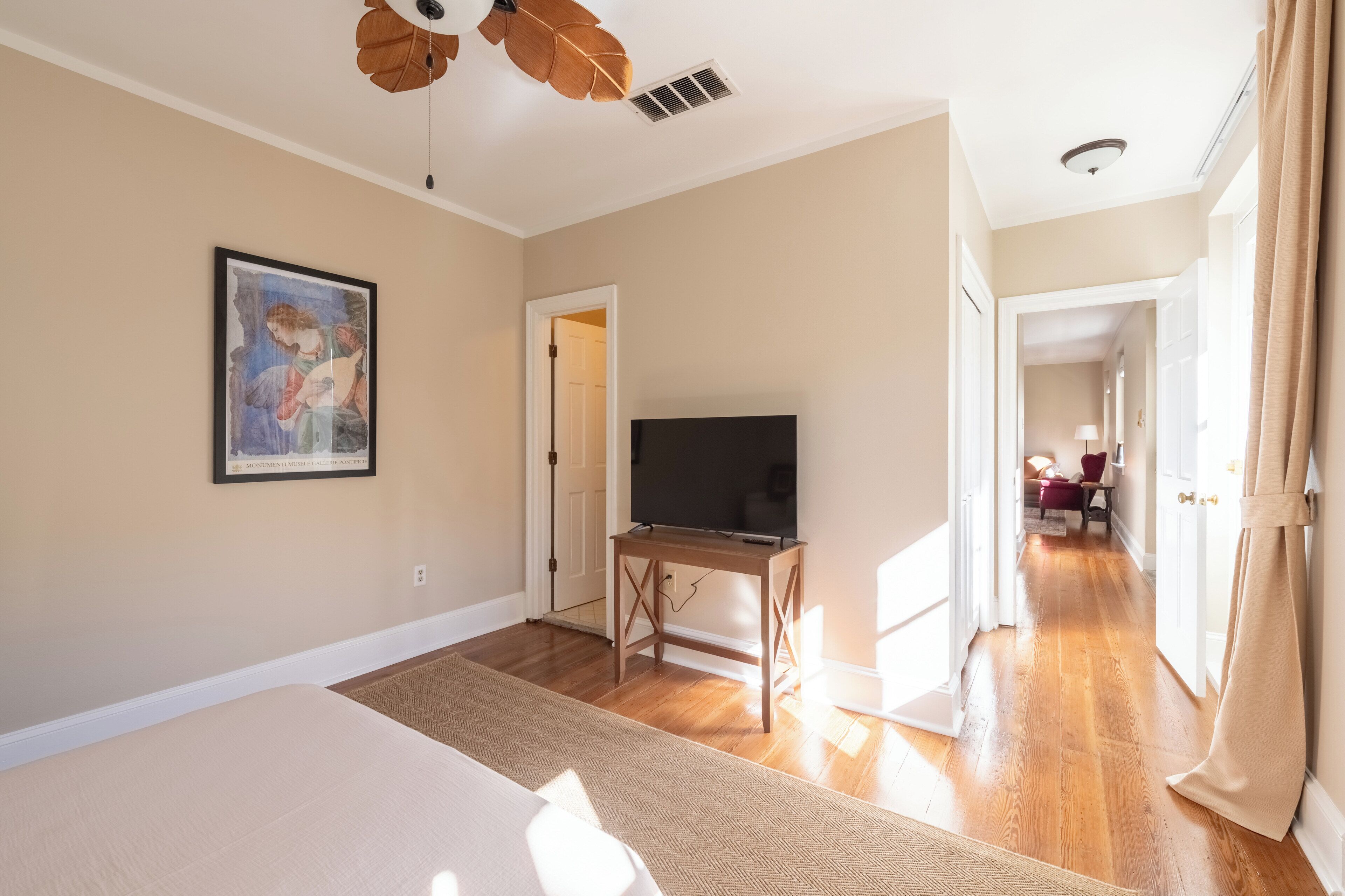 A spacious room with a large bed, a TV on a wooden stand, and a painting on the wall.