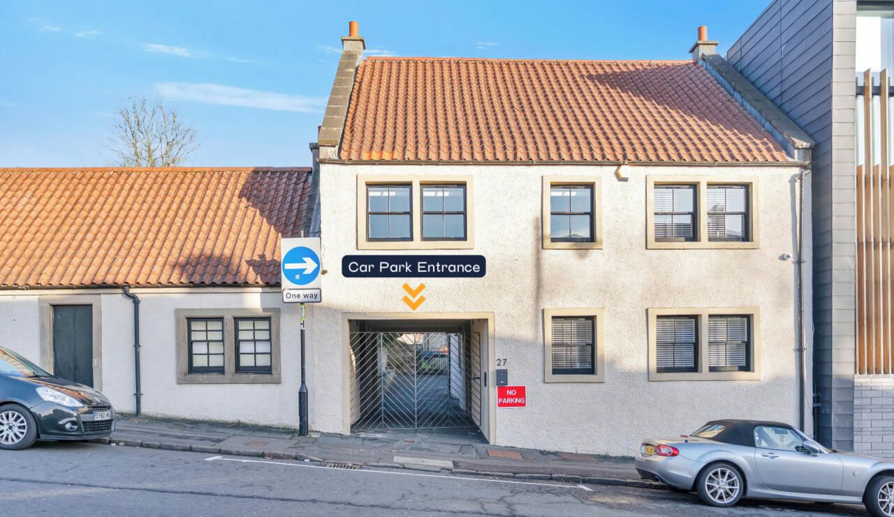 A building with a car park entrance, a one-way sign, and a no parking sign.