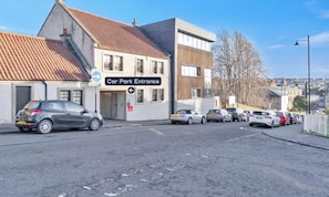 A car park entrance with a sign, a row of parked cars, and buildings in the background. - Comfortable 2 Bed Airdrie Flat w Private Parking (Airdrie)