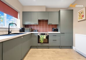 A modern kitchen with grey cabinets, a built-in oven, and a window with a red blind. - 3Bed House I Sleeps 6 I Dunfermline (Dunfermline)