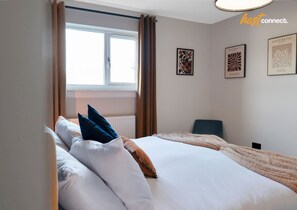 Une chambre d’hôtel avec un grand lit, une fenêtre avec des rideaux et deux œuvres d’art encadrées accrochées au mur.