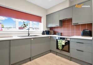 A modern kitchen with grey cabinets, a built-in oven, and a window with a red blind. - 3Bed House I Sleeps 6 I Dunfermline (Dunfermline)