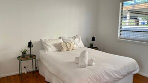 A bedroom with a bed, two bedside tables, a window with blinds, and a potted plant on one table. - Lookin Good is a short walk to Inyadda Beach (Manyana)