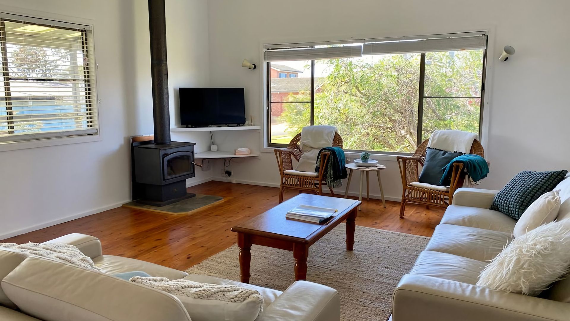 Ein Wohnzimmer mit Kamin, weißen Sofas, einem Fernseher und großen Fenstern.