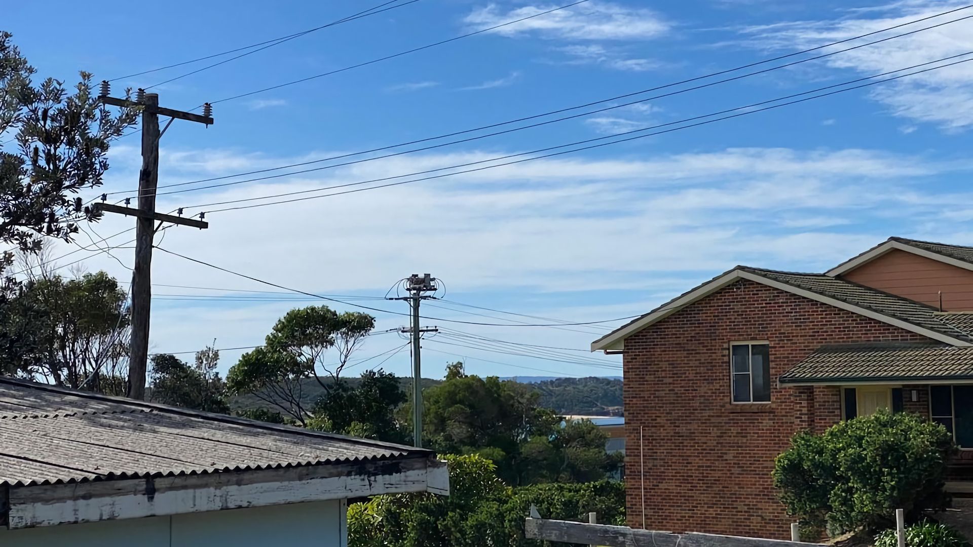 A residential area with a brick house, power lines, and a clear sky.