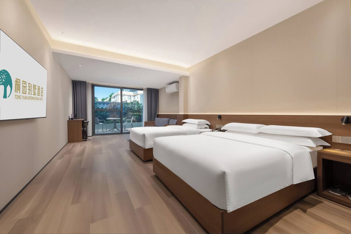 A hotel room with two beds, a desk, a chair, and a large window.