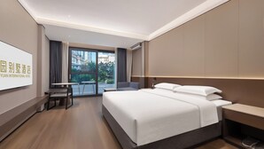 A hotel room with a large bed, a desk, and a chair, a television on the wall, and a view of buildings outside. - Tong Yuan International Hotel Guangzhou East Railway Station Meihuayuan Subway Station Branch  (Guangzhou)