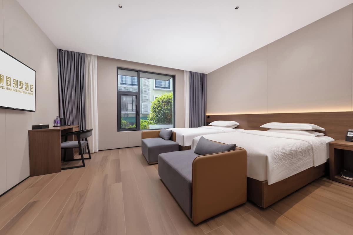 A modern hotel room with a large bed, a desk, a chair, and a small sofa.