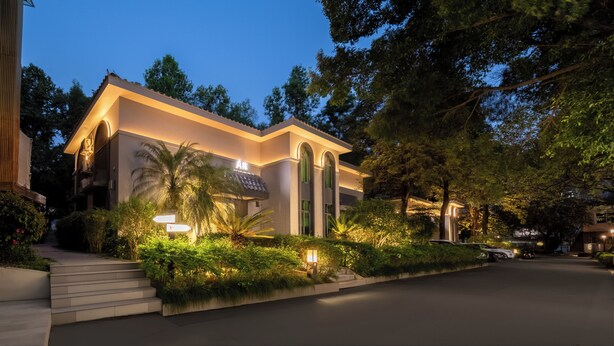 A modern hotel with a well-lit entrance, a staircase leading to the lobby, and lush greenery surrounding the property. - Tong Yuan International Hotel Guangzhou East Railway Station Meihuayuan Subway Station Branch  (Guangzhou)