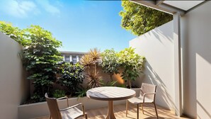 A patio with a round wooden table and two chairs, surrounded by various plants and a white wall. - Tong Yuan International Hotel Guangzhou East Railway Station Meihuayuan Subway Station Branch  (Guangzhou)