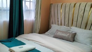 A neatly made bed with a striped headboard, a teal throw blanket, and a pillow with the word "Blessed" on it. - Paradise Apartments Embu (Embu)