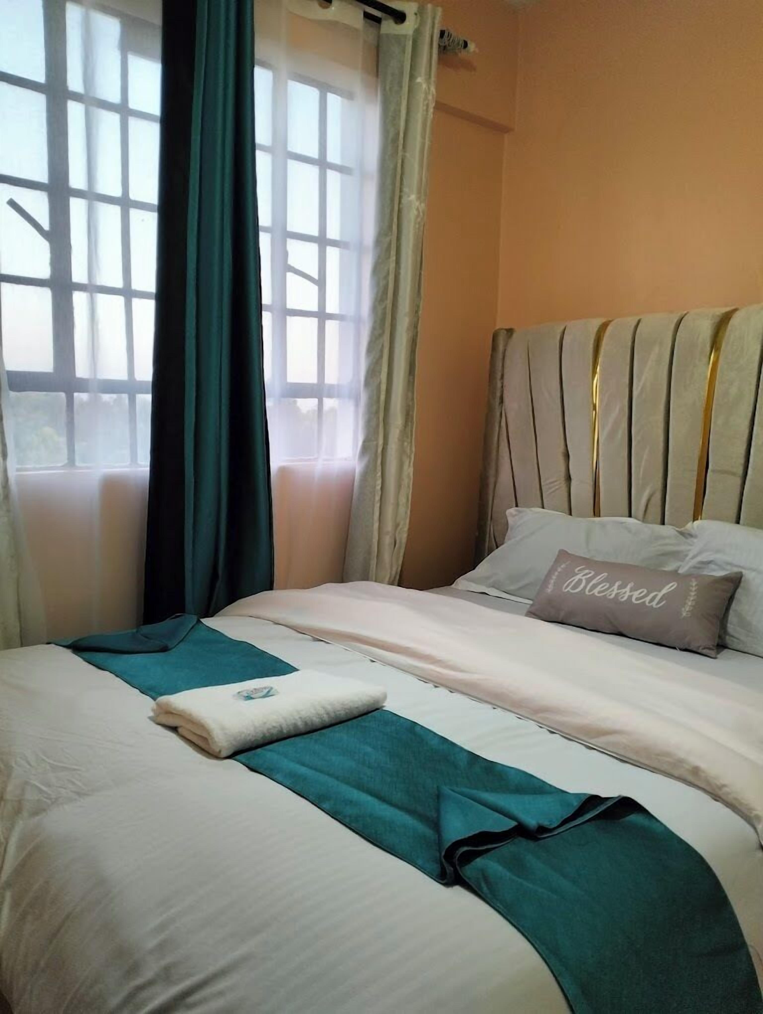 Camera d'albergo con un letto, una finestra con tende e un poggiatesta con un cuscino con la scritta 'Blessed'.