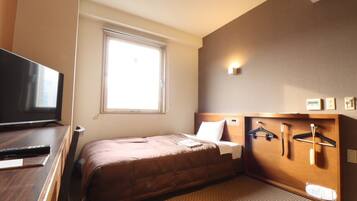 Habitación de hotel con cama, televisor, ventana y perchero en la pared.