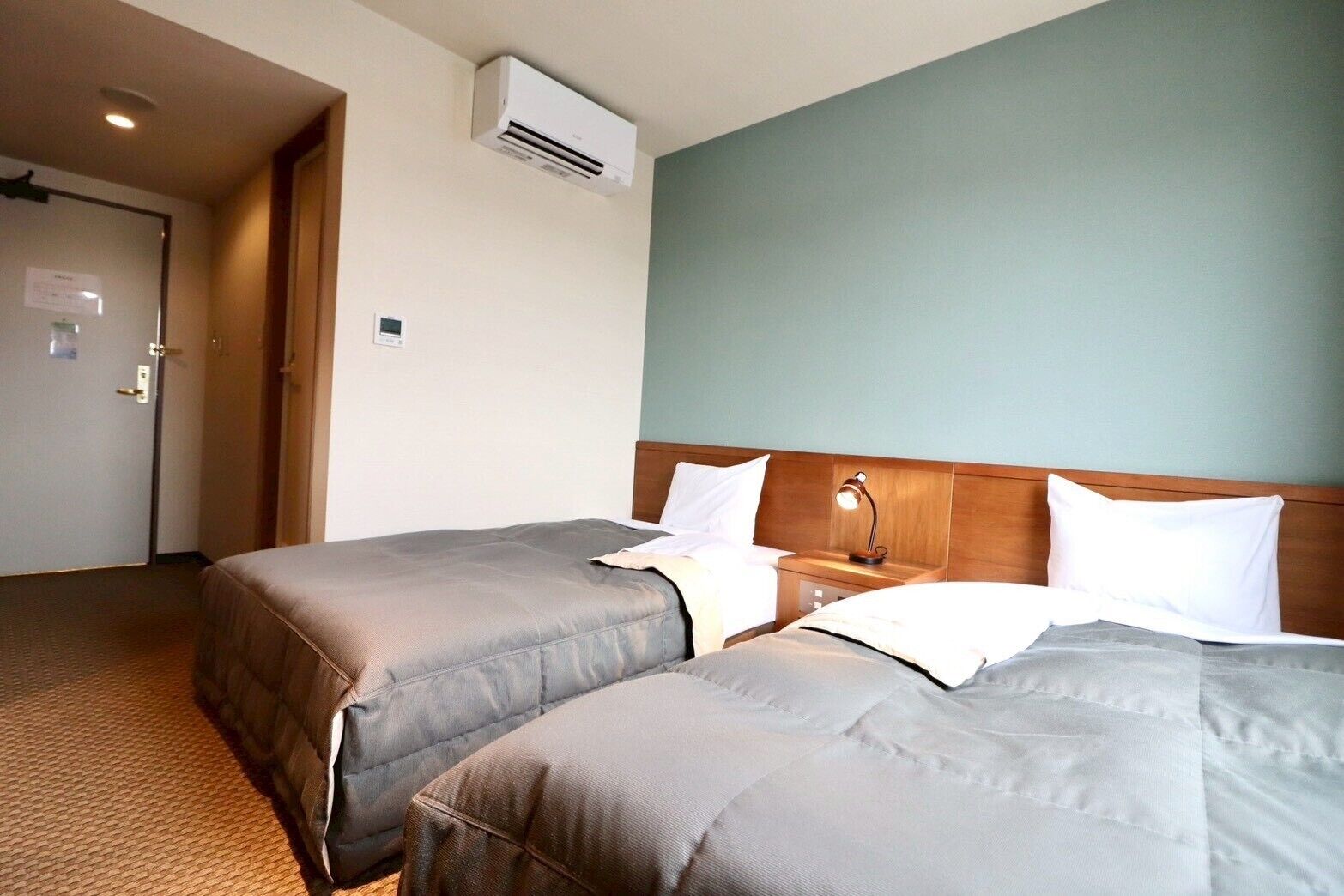 A hotel room with two beds, a wooden headboard, an air conditioning unit, and a door with a sign.