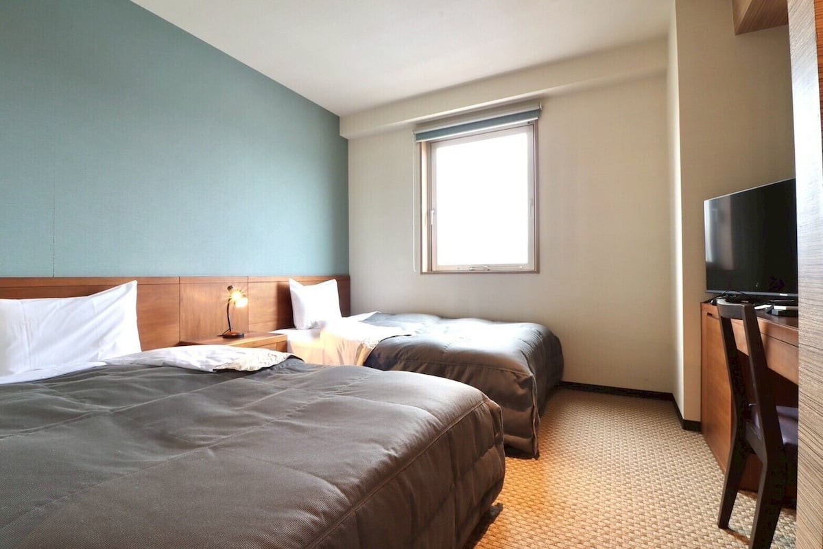 A hotel room with two beds, a TV, a desk, and a window.