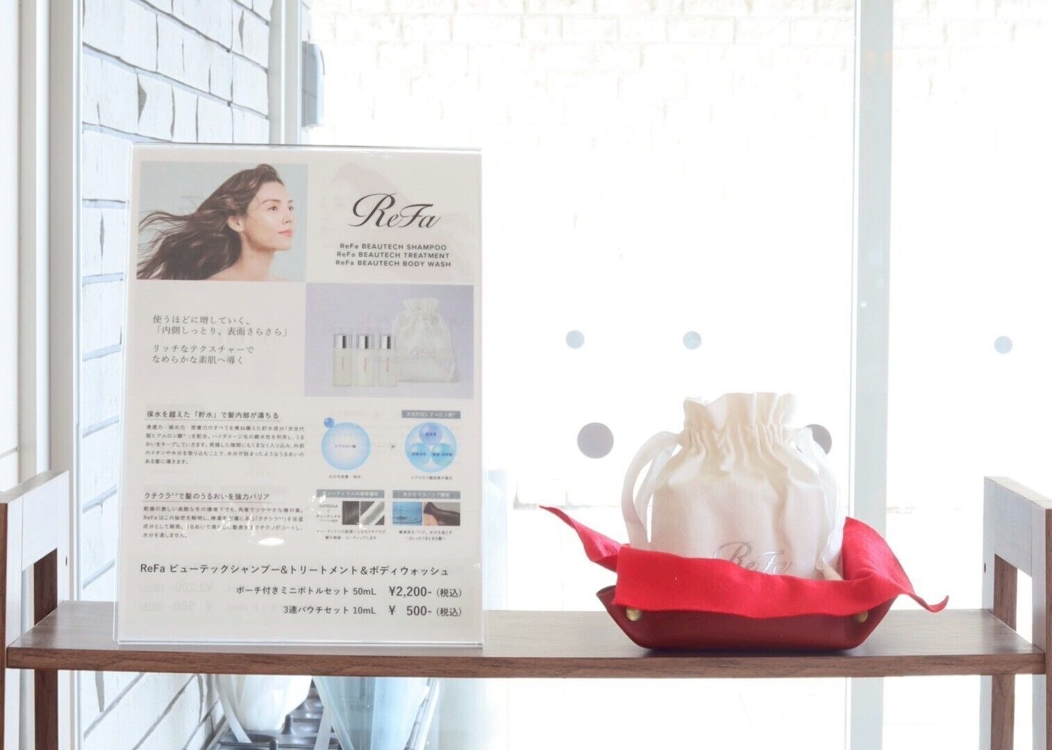 Productpresentatie van een ReFa BEAUTIQUE SHAMPOO en verzorgingsset voor het lichaam, inclusief een rode trekkoordtas, op een houten plank.