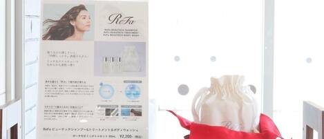 A product display with a ReFa BEAUTIQUE SHAMPOO and body wash set, including a red drawstring bag, on a wooden shelf.