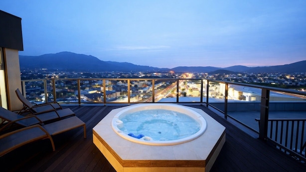 A hot tub on a wooden deck with a cityscape view at dusk. - HOTEL CUORE TSURUGA (Tsuruga)
