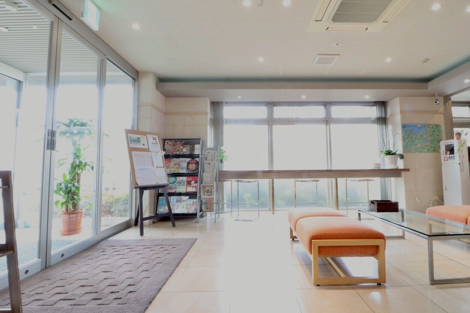 A spacious room with large windows, a reception desk, a bulletin board, and a seating area.