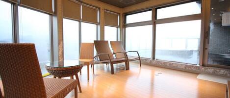 A room with large windows, wicker chairs, a glass table, and a wooden floor.