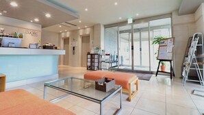 A hotel reception area with a glass table, orange seating, a reception desk, and a view of the outside through glass doors. - HOTEL CUORE TSURUGA (Tsuruga)