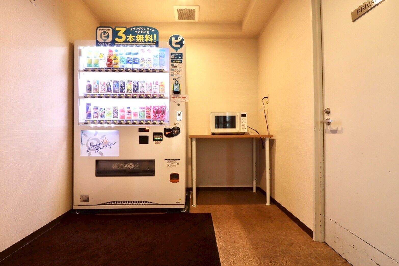 A vending machine in a hallway with a microwave on a small table.