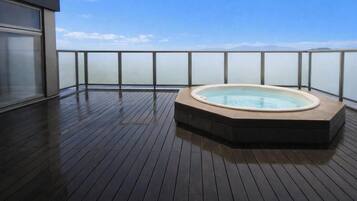 A hot tub on a wooden deck with a view of the sea and mountains.