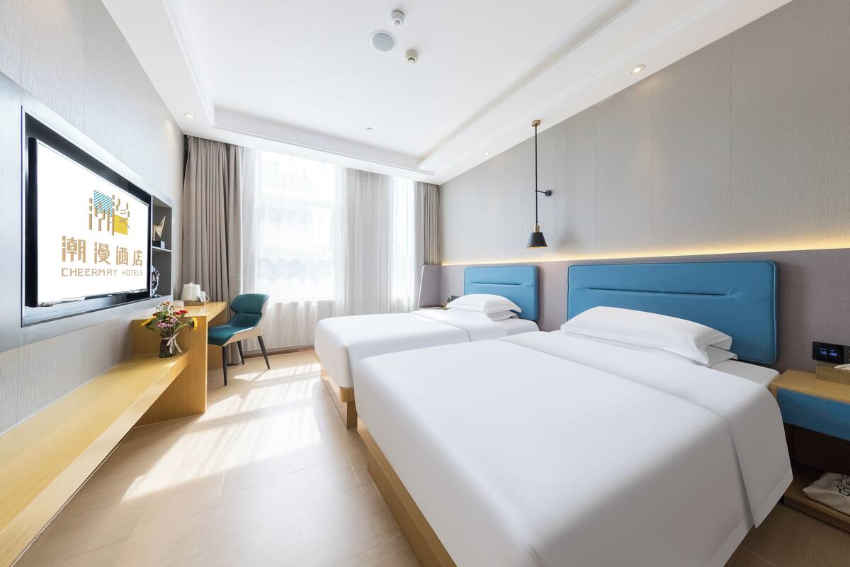 A hotel room with two beds, a desk, a chair, a TV, and a window with curtains.