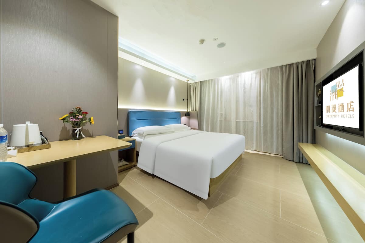 A hotel room with a bed, a desk, a chair, a TV, and a window with curtains.