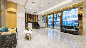 Eine moderne Lobby mit einer Rezeption, einer Sitzecke und Blick auf die Straße durch große Glasüren.