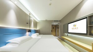 Ein Hotelzimmer mit zwei Betten, einem an der Wand montierten Fernseher und einem Schreibtisch mit Lampe.