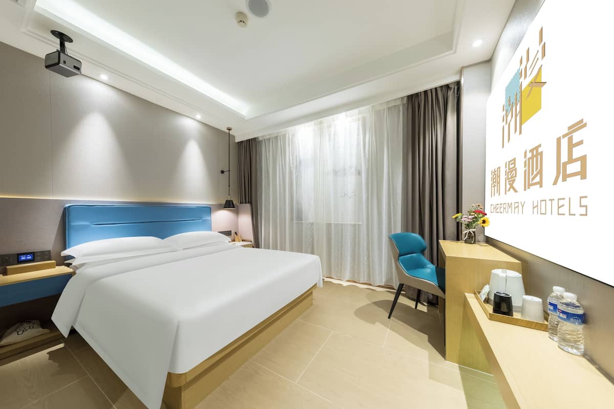 A hotel room with a large bed, a desk with a chair, a nightstand, and a wall-mounted TV.