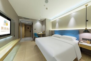 Ein Hotelzimmer mit einem großen Bett, einem Schreibtisch mit Stuhl, einem an der Wand montierten Fernseher und einer Deckenleuchte.