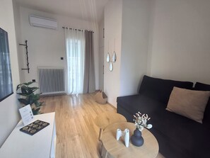 A modern living room with a black sofa, a round wooden coffee table, a small plant, and a vase with flowers.