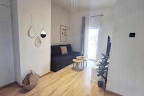 A living room with a sofa, a small round table, a hanging plant, and a framed botanical print on the wall.