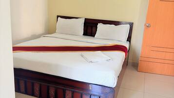 Una cama con cabecera de madera, ropa de cama blanca y un toque de color rojo.