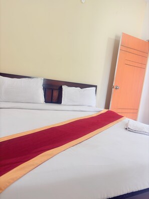 A neatly made bed with white linens, a red and yellow bed runner, and a wooden headboard. - SS Home Stay (Bengaluru)