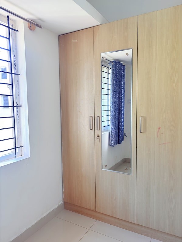 Une pièce avec une armoire en bois, une fenêtre avec des barreaux en métal et un miroir.