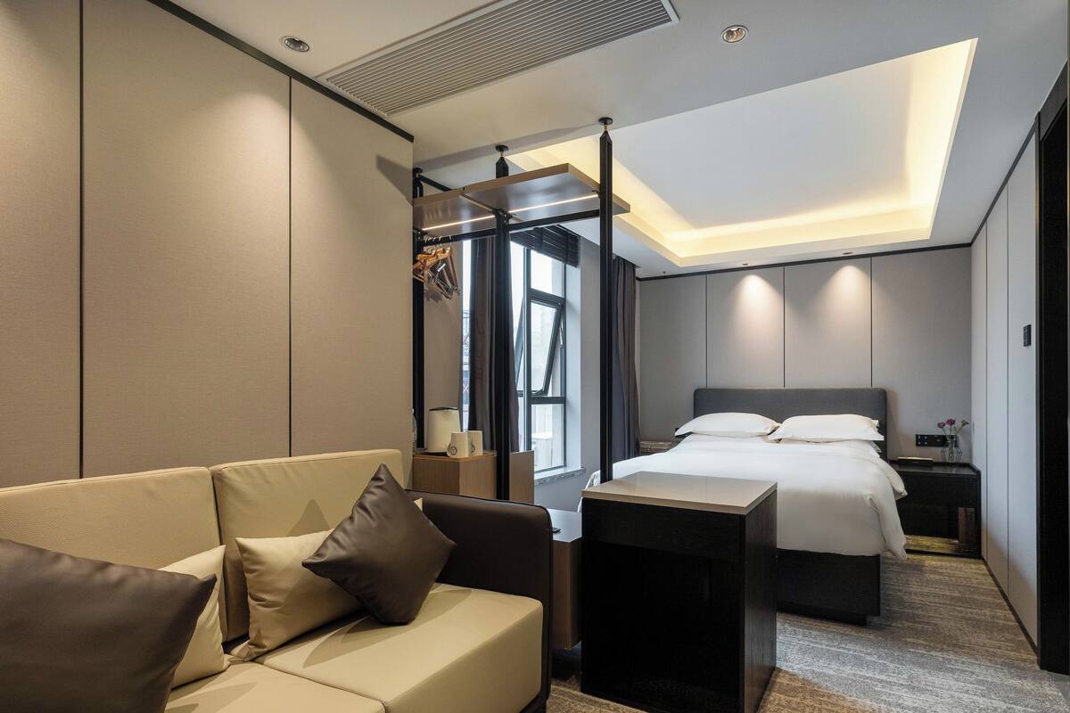 A modern hotel room with a sofa, a bed, a nightstand, and a small table.