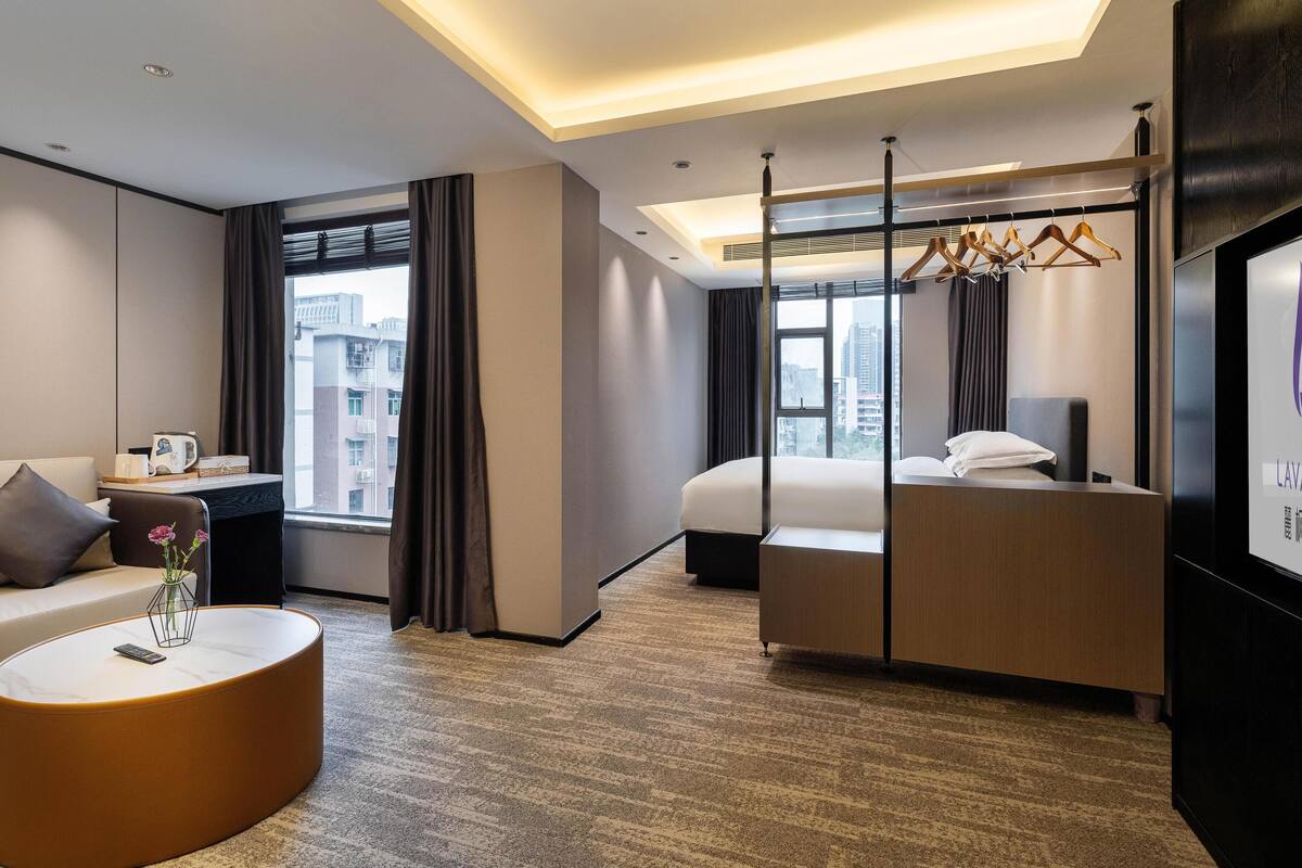 A modern hotel room with a bed, a sofa, a small table, and a TV.