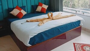 A hotel room with a large bed, teal walls, and a view of trees through the window. - Rudraksh Resort (Mussoorie)