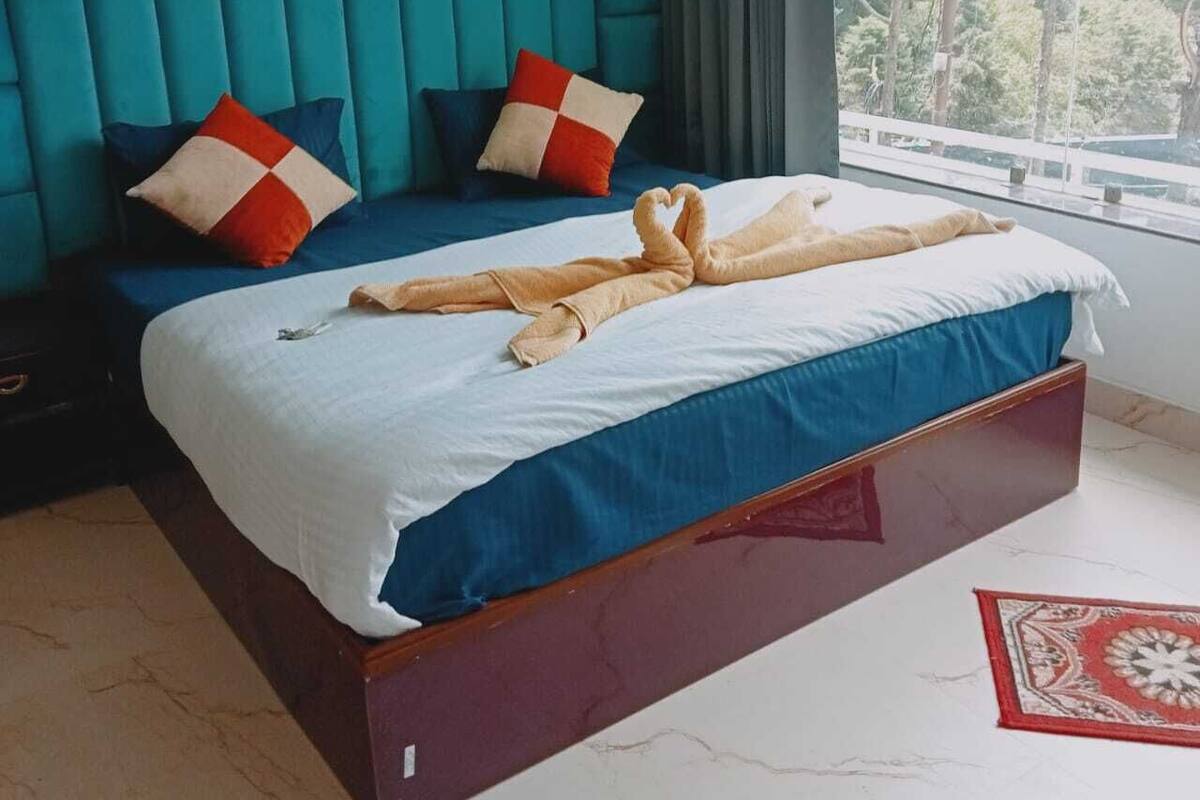 A hotel room with a large bed, teal walls, and a view of trees through the window.