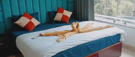 A hotel room with a large bed, teal walls, and a view of trees through the window.